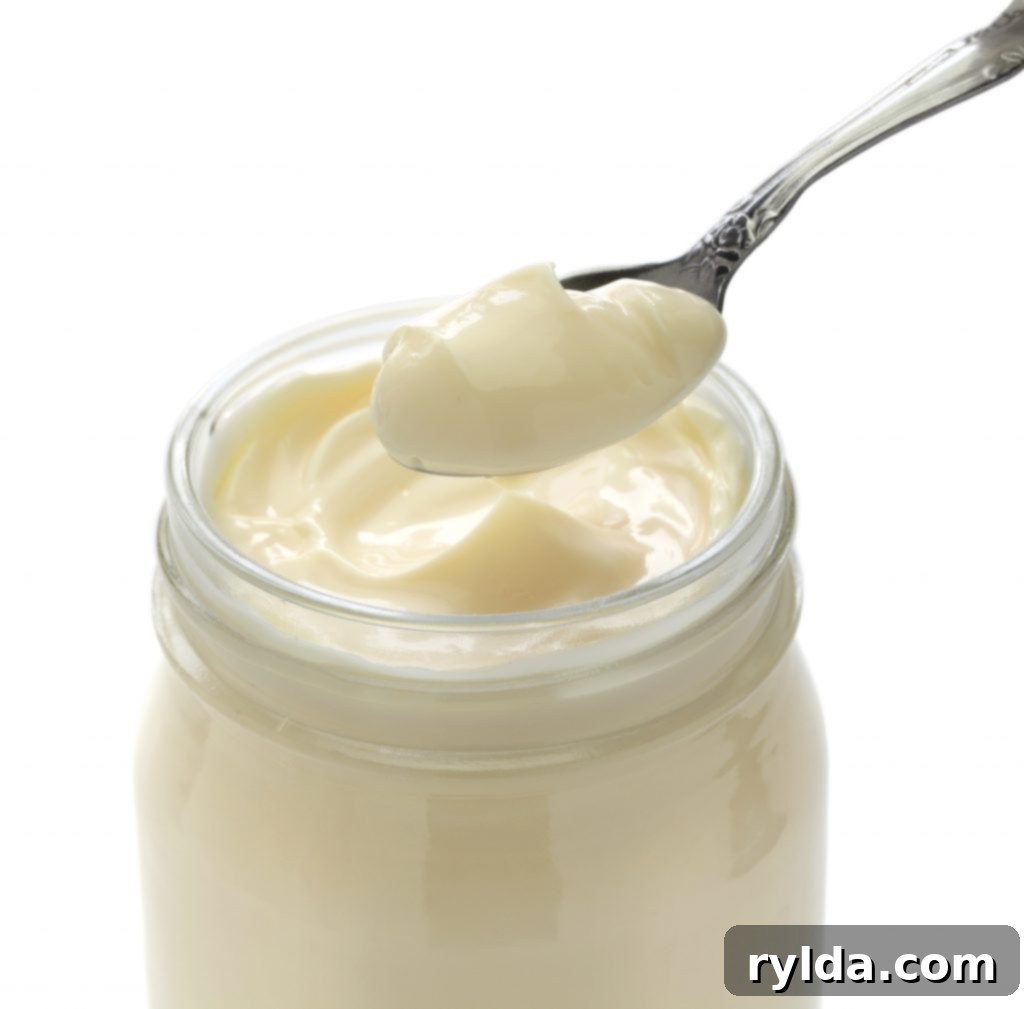 A spoon scooping creamy mayonnaise from a jar, highlighting a key ingredient for juicy chicken burgers.