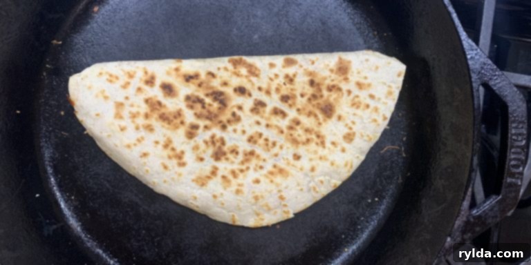 Half-folded chicken quesadilla cooking in a skillet