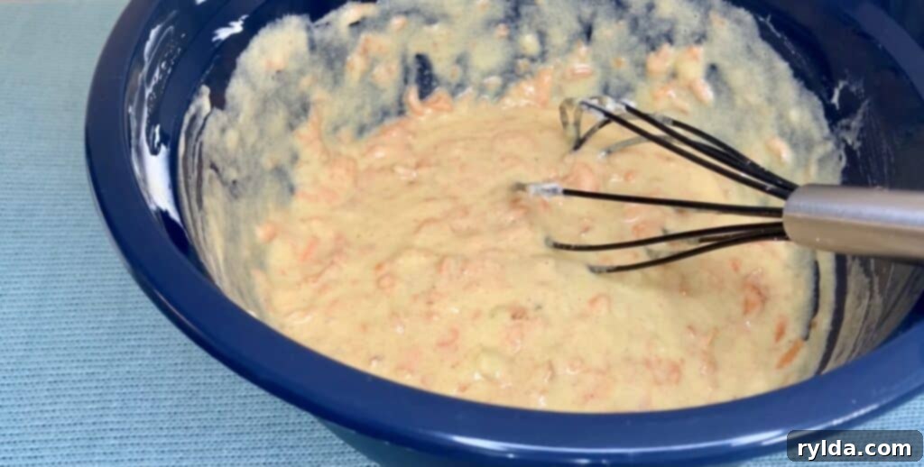 A bowl containing all the mixed wet ingredients for the banana carrot loaf, including mashed banana, grated carrots, and sour cream, ready for dry ingredients.