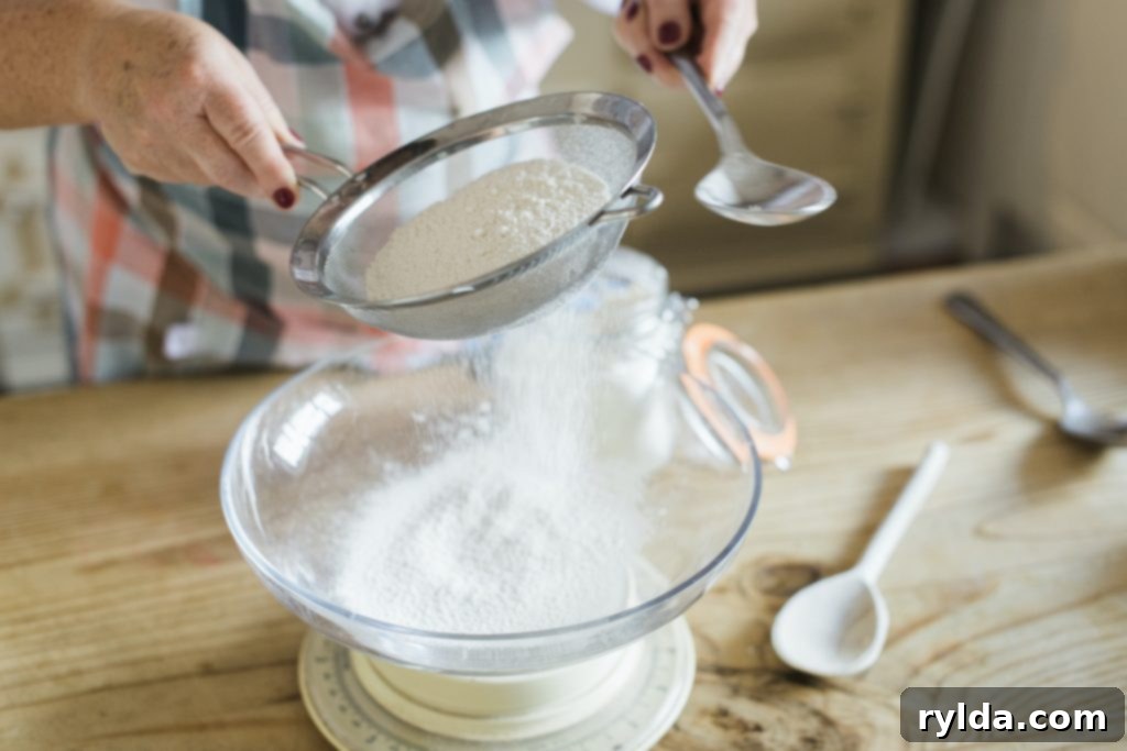 Close-up of flour being sifted into a bowl, creating a fine, powdery texture, essential for light and fluffy cookies.