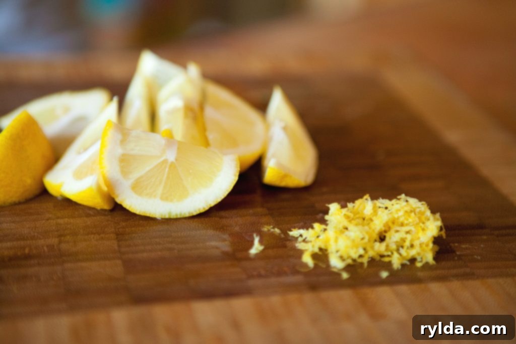 Close-up of fresh lemons and finely grated lemon zest on a cutting board, ready for incorporating into the glaze.